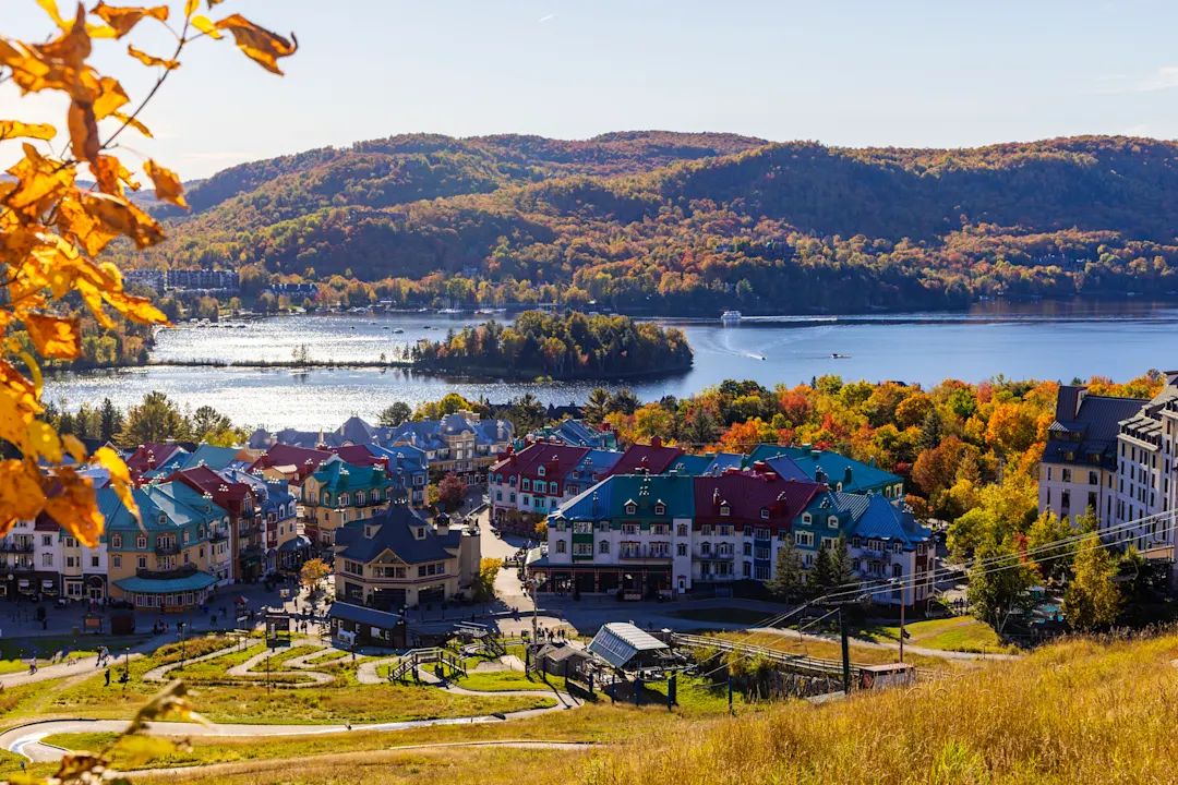 Herbstliche Aussicht auf ein Bergdorf mit bunten Häusern, einem glitzernden See und bewaldeten Hügeln in Herbstfarben.