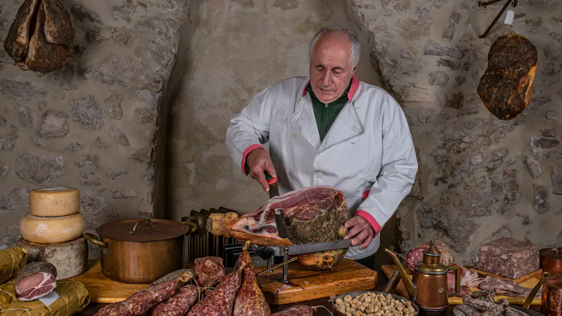 Italien, Salumeria Fleischer schneidet frischen Schinken und symbolisiert damit Kulinarikreisen nach Italien.