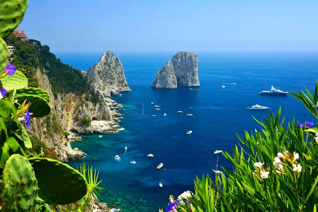 Capri, Italien Blick auf die Küste von Capri mit den Faraglioni-Felsen, Blumen und Booten im blauen Meer in Italien