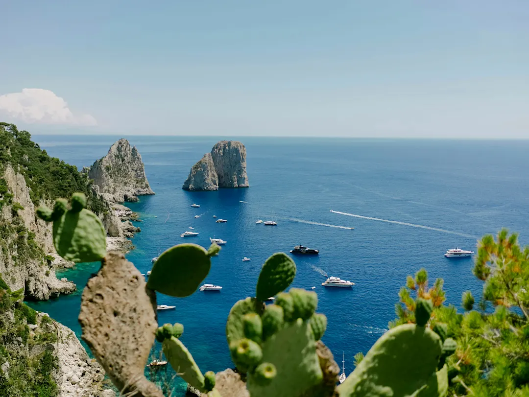 Capri, Italien Blick auf die Küste von Capri mit den Faraglioni-Felsen, Blumen und Booten im blauen Meer in Italien