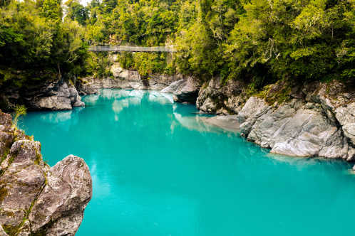 Das türkisfarbene Wasser des Hokitika River fließt unter einer Drehbrücke an diesem beliebten Touristenziel in der Nähe von Hokitika, Aotearoa Neuseeland.