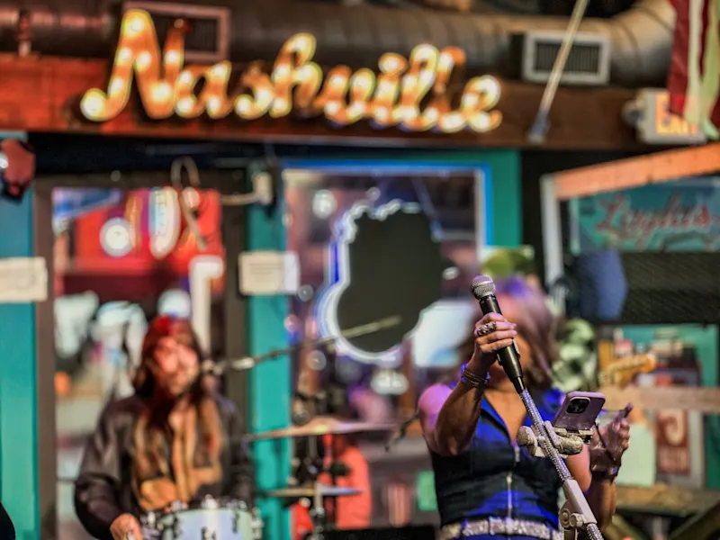 Live-Musik in einer Bar mit unscharfem "Nashville"-Schild im Hintergrund. Nashville, Tennessee, USA.