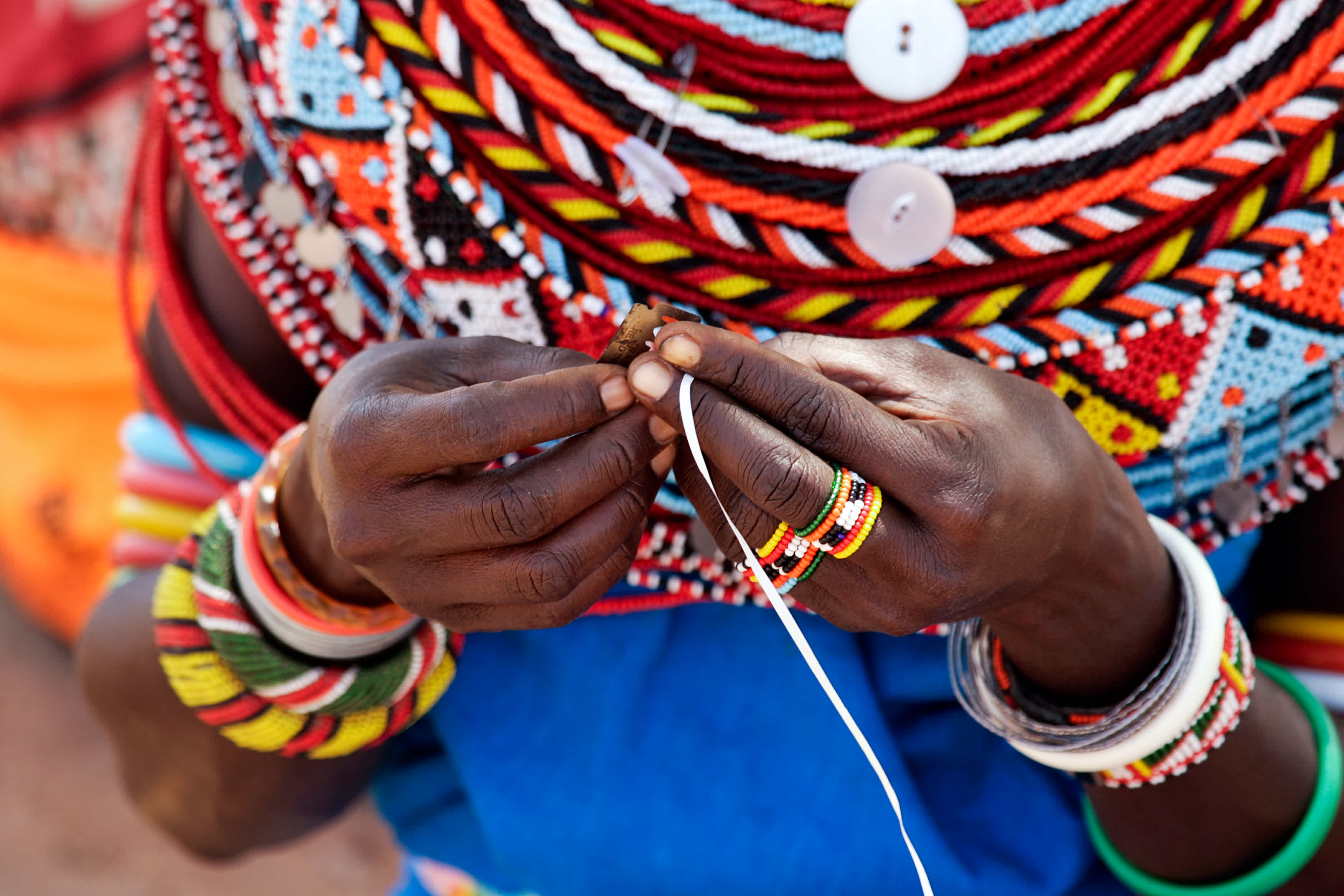 Gros plan sur les mains d'une femme Samburu en train de tisser des perle au Kenya.