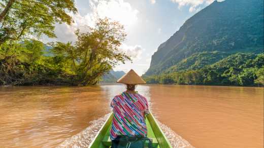 Frau mit traditionellem Hut auf dem braunen Wasser des Flusses Nam Ou in Laos.