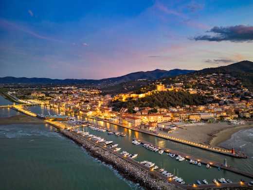 Luftbild des Yachthafens in Castiglione della Pescaia bei Abenddämmerung mit Hügellandschaft im Hintergrund