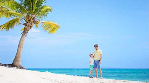 Vater und Sohn am Strand mit Palme im Hintergrund.
