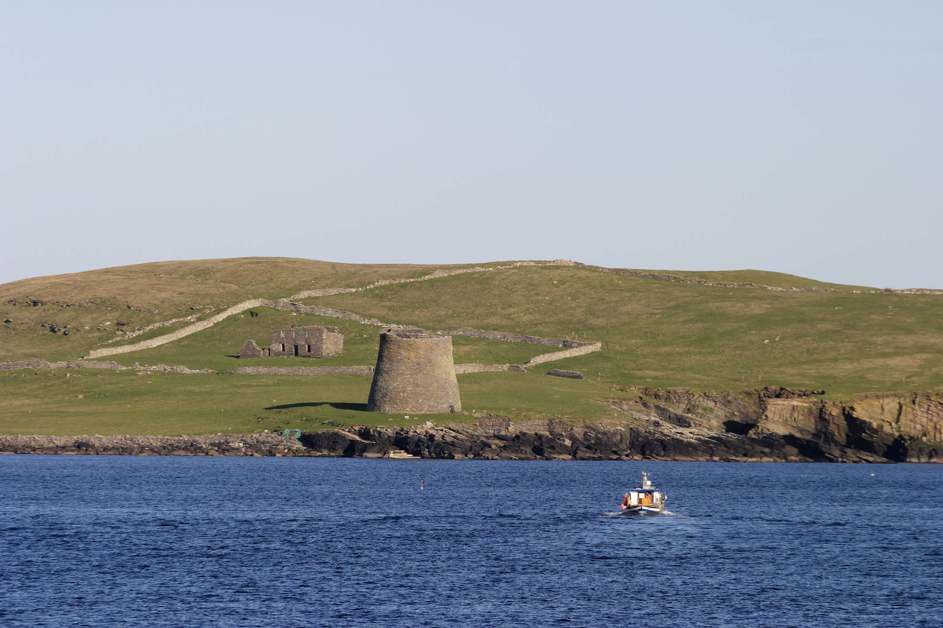 Bateau en mer avec la tour viking sur une petite île en arrière-plan, îles Shetland, en Écosse