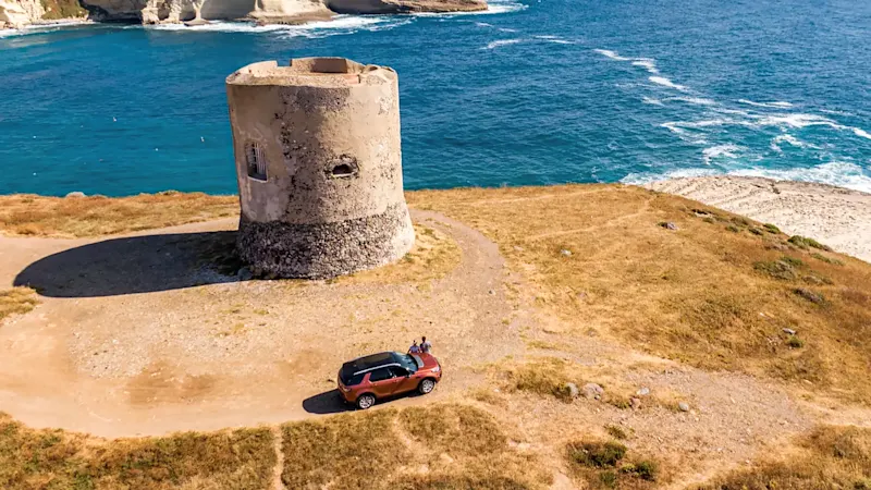 Italien, Sardinien, Roadtrip Turm am Rande einer Klippe in Sardinien und zwei Menschen am Auto als Symbolbild für einen Roadtrip durch Italien. Sardinien, Italien