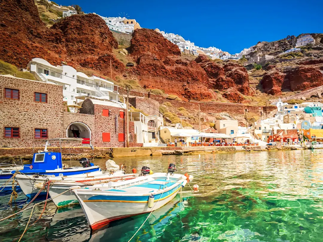 Bunte Häuser an roten Klippen mit Fischerbooten. Ammoudi-Bucht, Santorin, Kykladen, Griechenland.