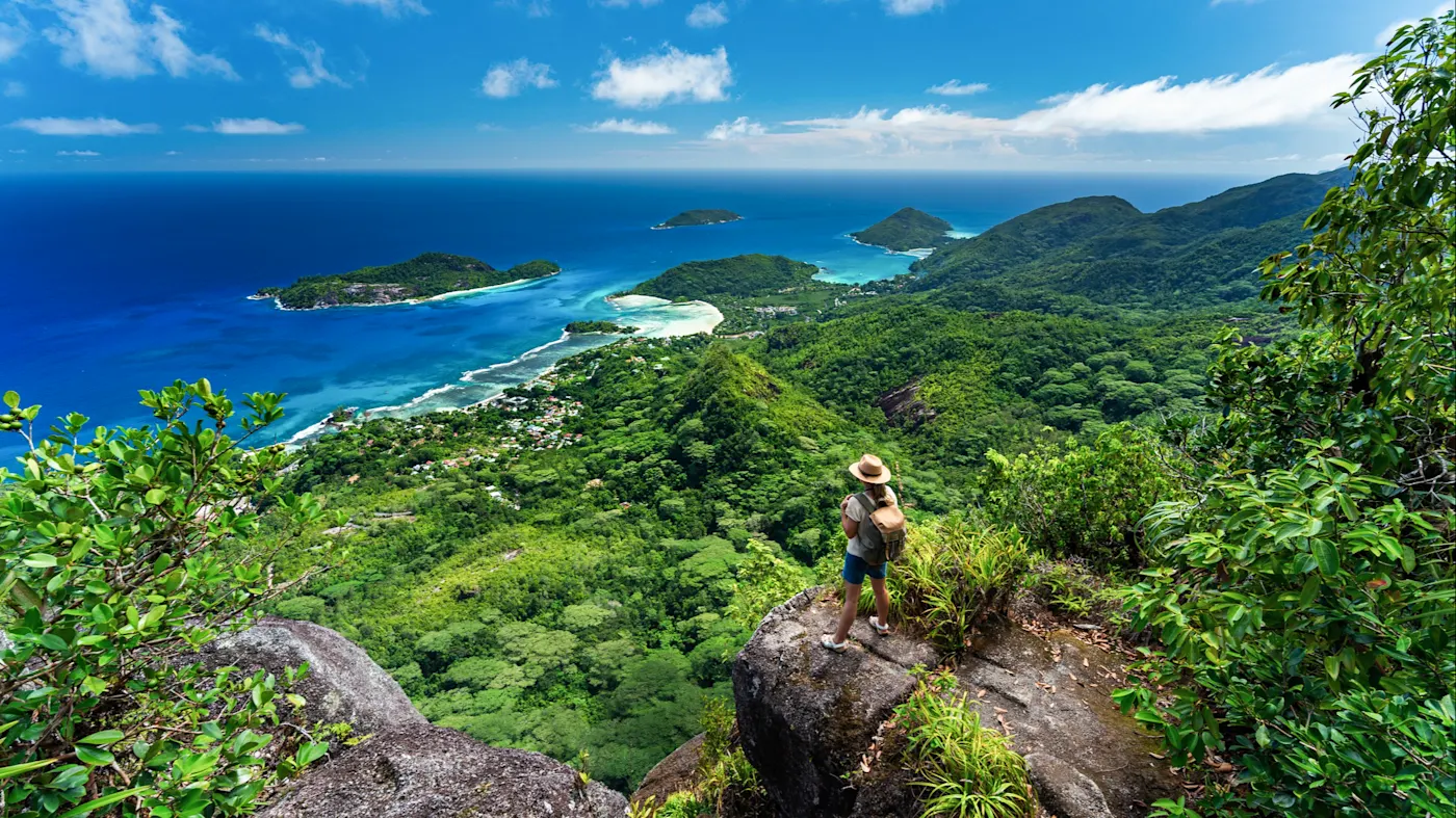 Seychellen, Mahe Wanderin auf einem Felsen mit Blick auf die tropische Küste und das blaue Meer. Mahé, Seychellen.