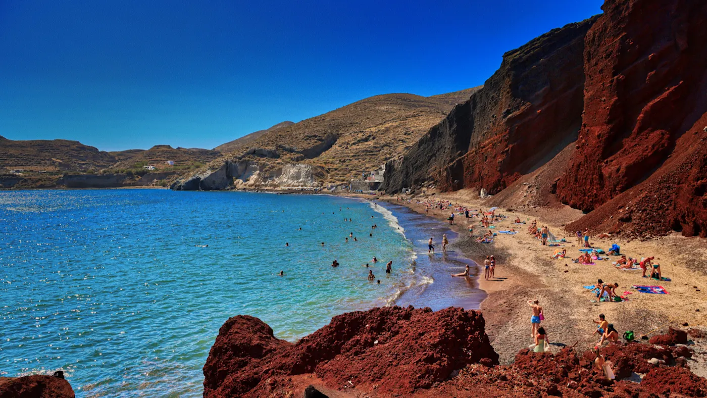 Akrotiri, Santorini, Griechenland Roter Sandstrand mit Badegästen und steilen Klippen unter blauem Himmel, Akrotiri, Santorini, Griechenland