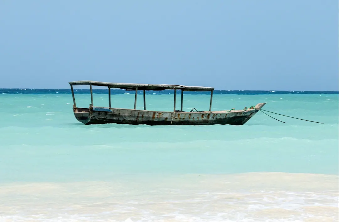 Traditionelles Holzboot treibt im türkisblauen Wasser vor einem Sandstrand. Pemba Island, Sansibar, Tansania.
