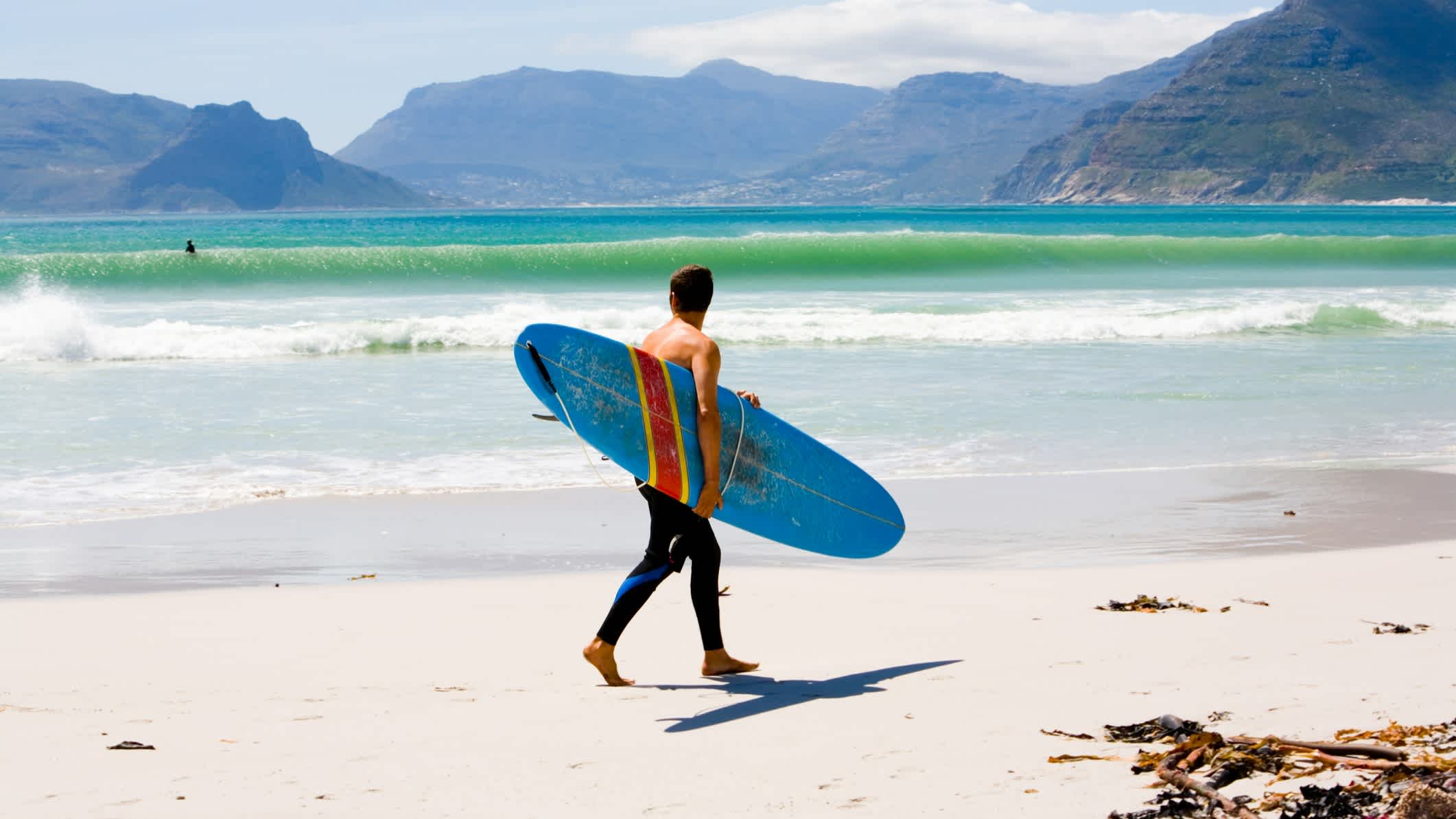 Un surfeur avec une planche de surf en train de marcher sur la plage.