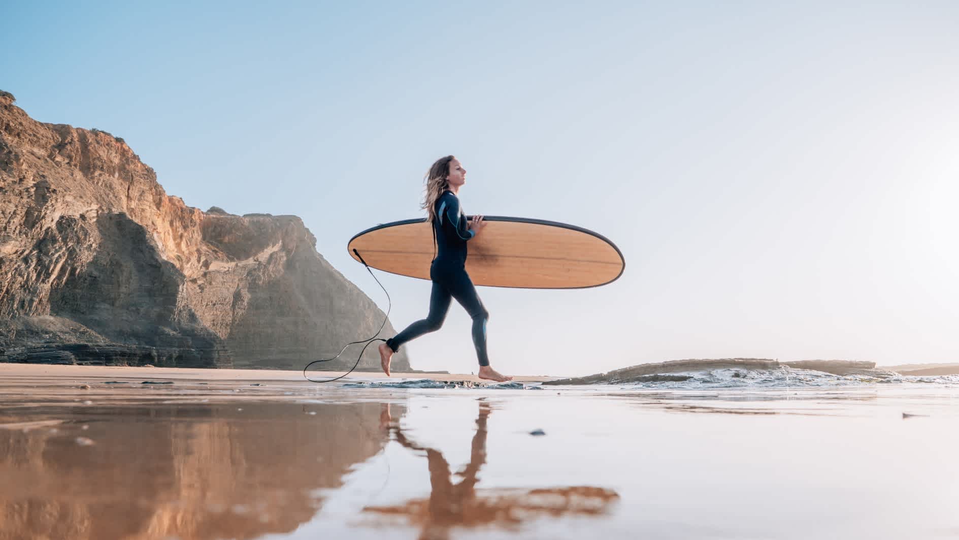 Surfen läuft mit Surfbrett unterm Arm auf das Meer zu