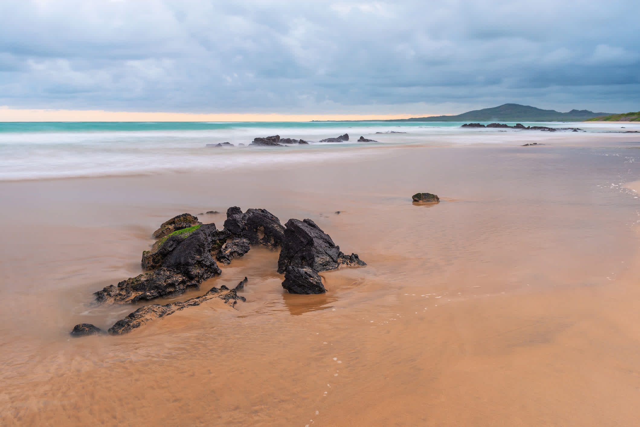 Rocher sur le sable de la plage de Puerto Villamil au coucher du soleil, sur l'île d'Isabela, Parc national des Galapagos, Équateur.