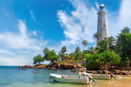 Bateau blanc au bord de l'eau avec vue en arrière-plan du phare blanc de Dondra Head près de Matara, Sri Lanka.