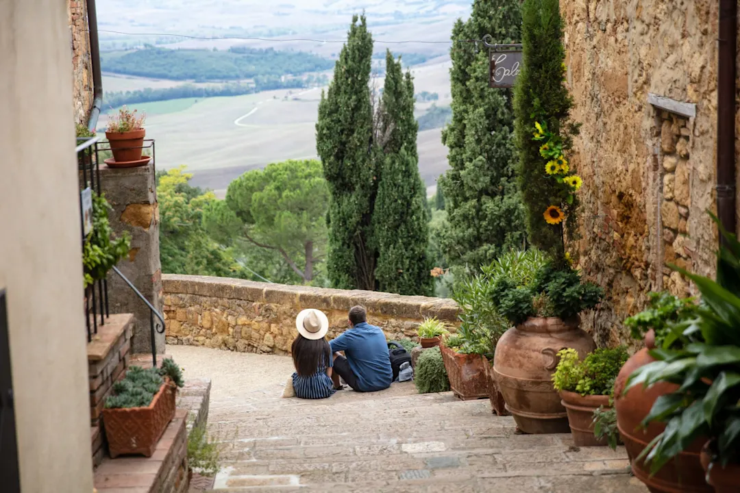 Italien, Toskana, Pienza Paar sitzt auf einer Treppe in einer Gasse mit Blick auf eine toskanische Landschaft