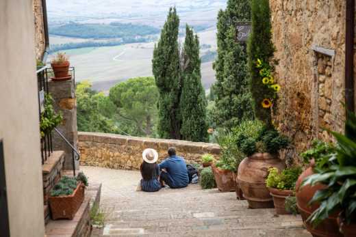 Paar sitzt auf einer Treppe in einer Gasse mit Blick auf eine toskanische Landschaft
