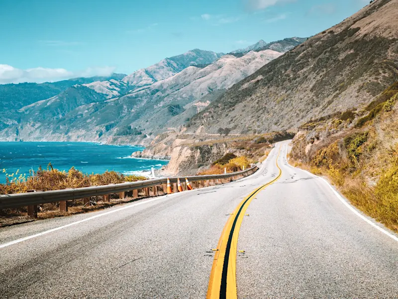 Küstenstraße mit Blick auf das Meer und Berge bei klarem Himmel. Big Sur, Kalifornien, USA.
