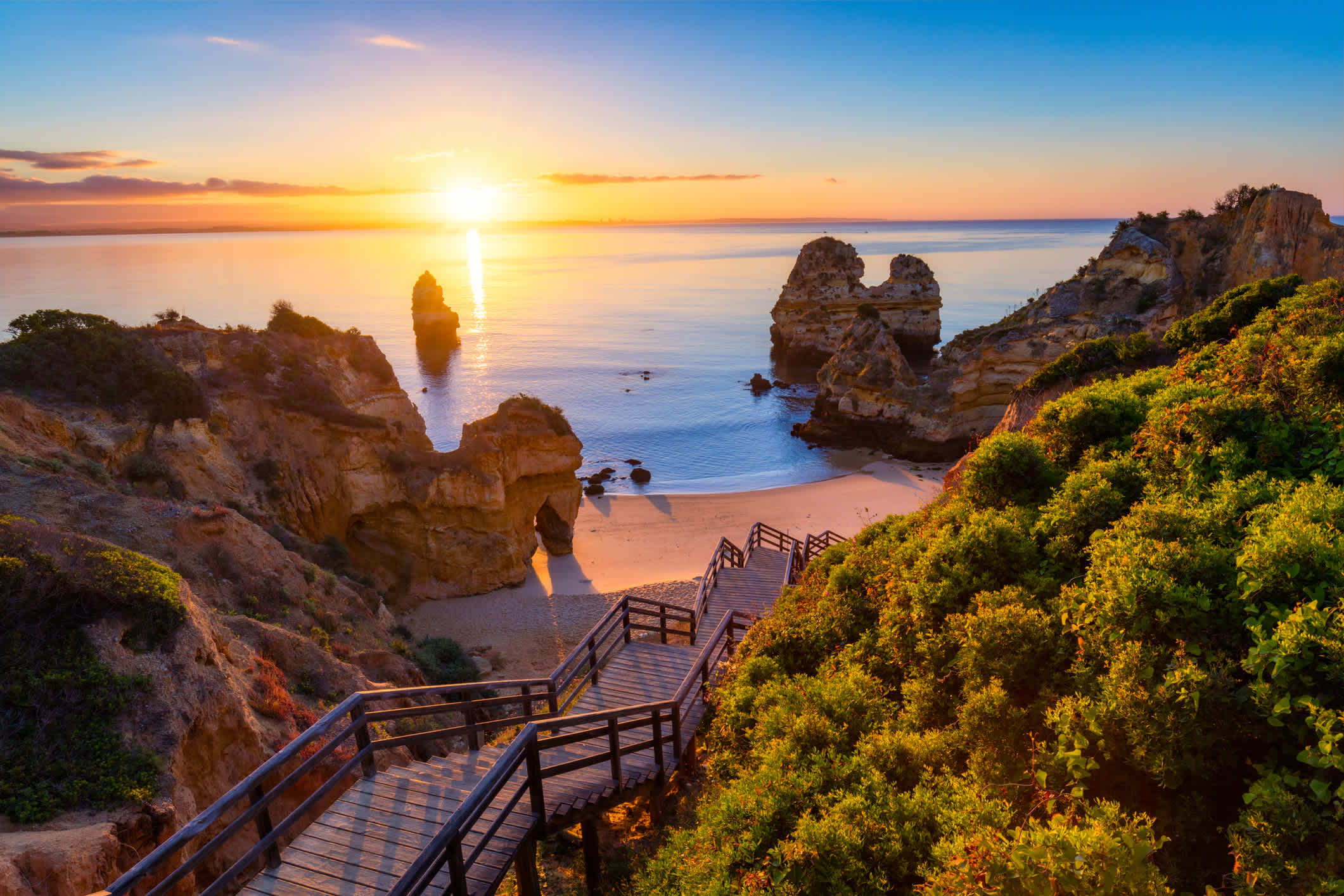 Sonnenaufgang am Camilo Strand in Lagos, Algarve, Portugal. Holzsteg zum Strand Praia do Camilo, Portugal. Malerische Aussicht auf den Strand Praia do Camilo in Lagos, Algarve Region, Portugal.