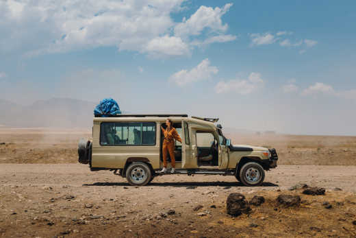 Glückliche Entdeckerin im Safari-Jumpsuit im modifizierten Jeep-Safari-Auto bei einem Roadtrip im Serengeti-Nationalpark, Tansania
