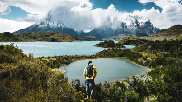 South America, Chile, Patagonia, view of a hiker in Torres del Pain with a sweeping view of snowy mountains, glacial lakes, and forest.
