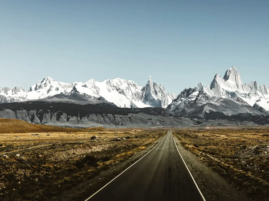 Argentinien, Santa Cruz, El Chaltén Gerade Straße mit schneebedeckten Bergen im Hintergrund. El Chaltén, Santa Cruz, Argentinien.