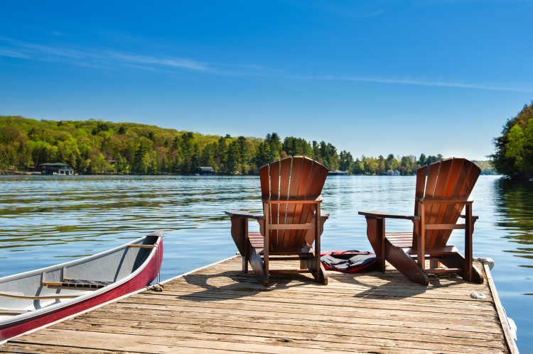 Un canoë rouge et deux chaises longues sur une jetée en bois surplombant les eaux bleues d'un lac à Muskoka, en Ontario, au Canada.