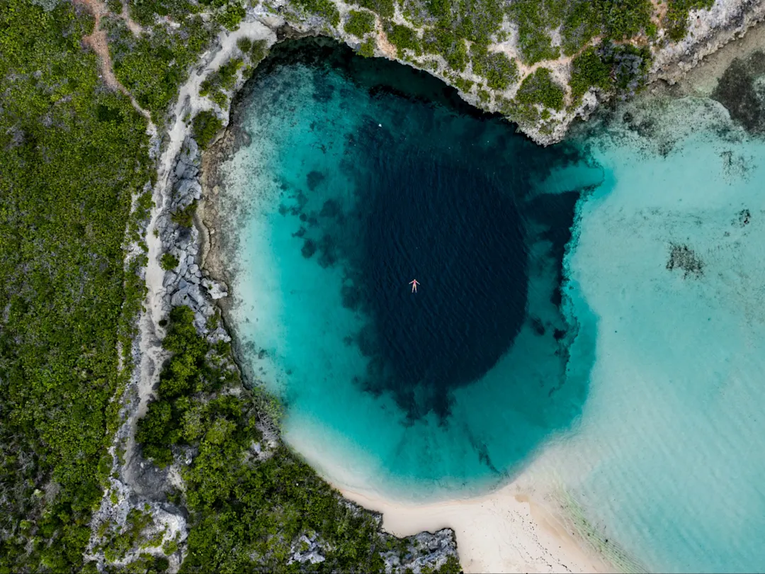 Luftaufnahme eines Schwimmers in einem kreisrunden, tiefblauen Wasserloch auf Long Island, Bahamas.