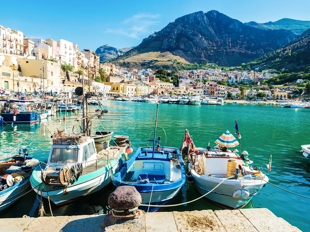 Fischerboote im türkisfarbenen Wasser des Hafens mit Blick auf die Altstadt. Castellammare del Golfo, Sizilien, Italien.