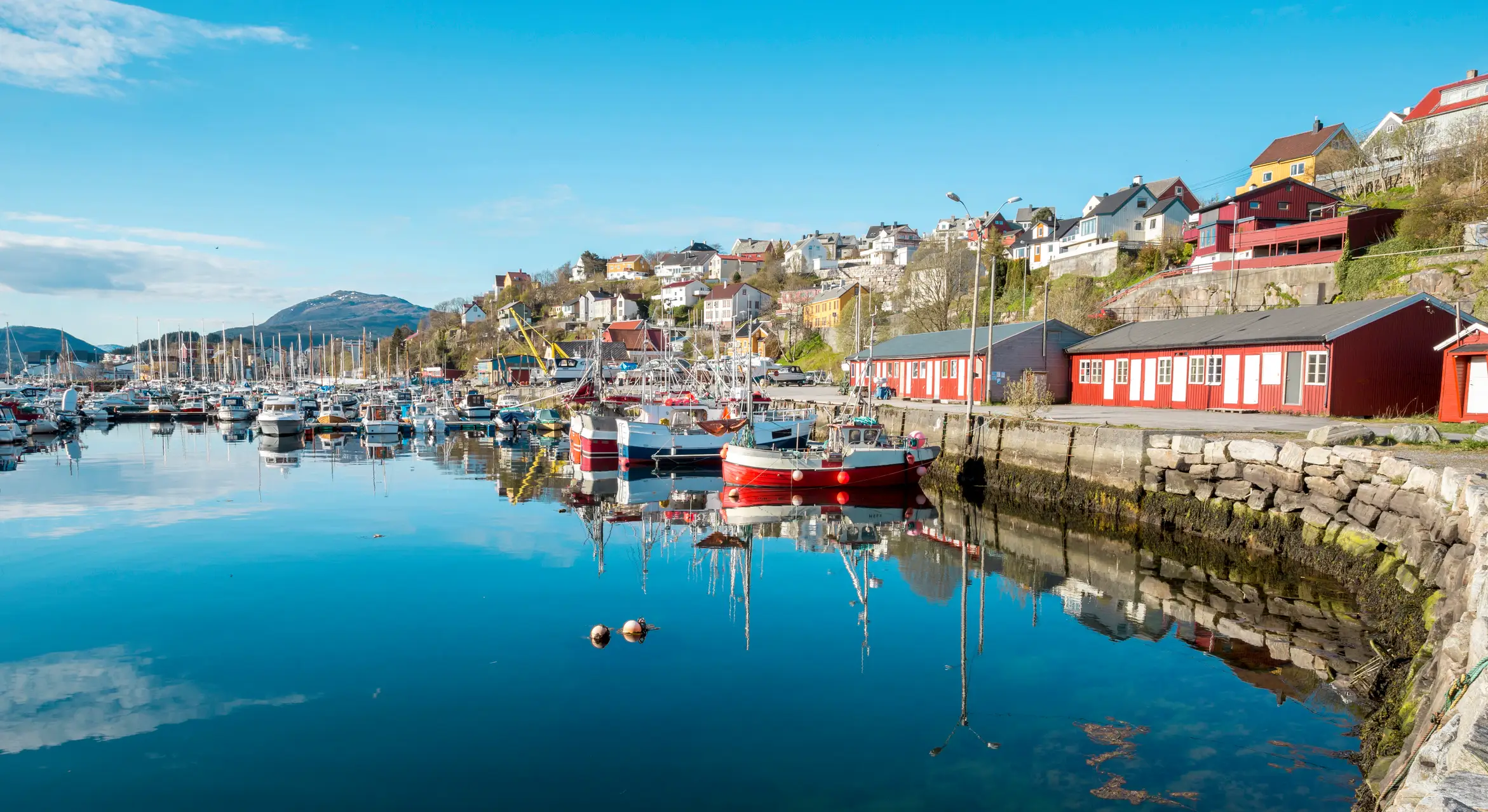 Kleine Boote im Hafen von Kristiansund und Holzhäuser entlang der Küste an einem heiteren Tag