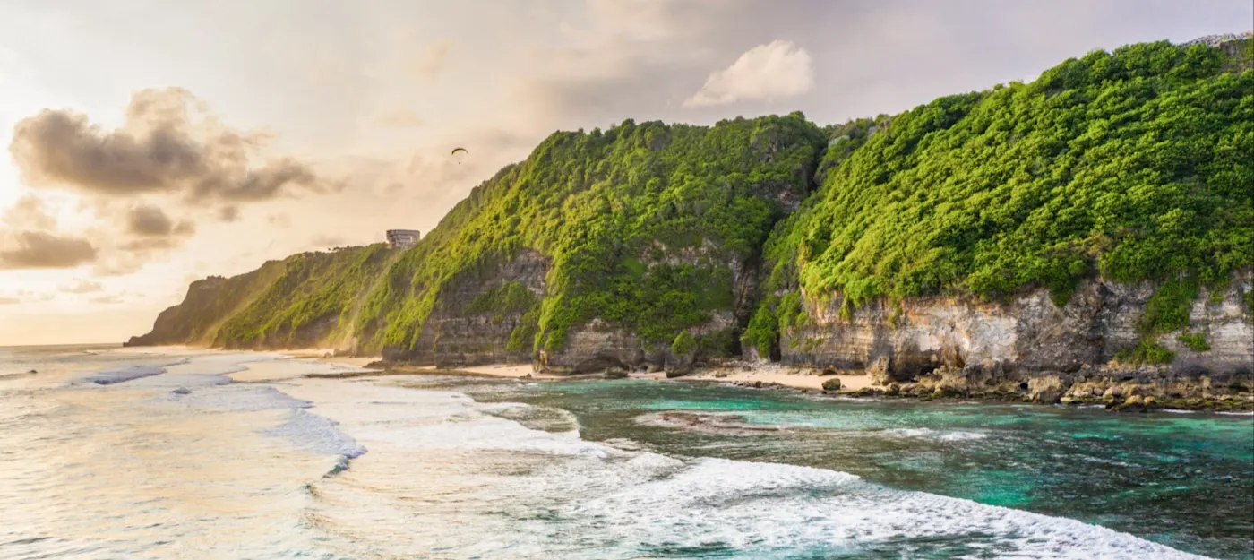 Uluwatu, Bali, Indonesien Steile, grüne Klippen mit Sandstrand und türkisfarbenem Wasser bei Sonnenuntergang. Uluwatu, Bali, Indonesien.
