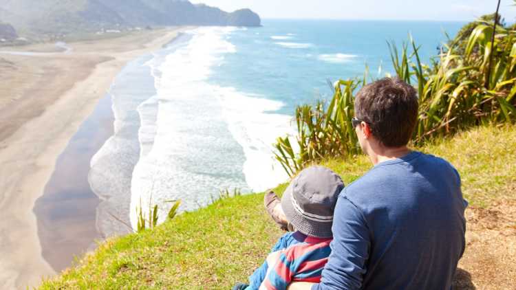 Vater und Sohn beobachten einen Strand in Neuseeland.