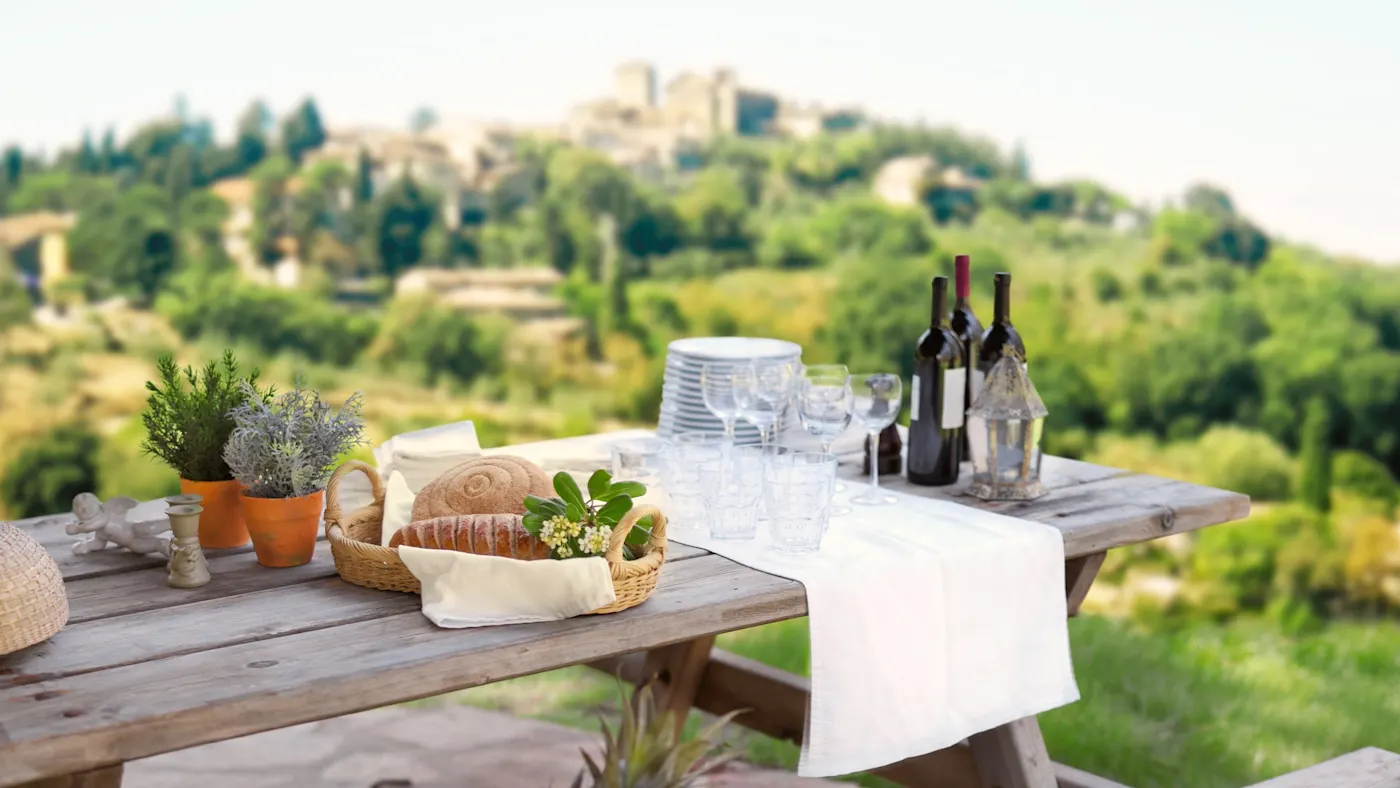 Italien, Toskana,, Kulinarik Rustikale Holzbank mit Picknick aus Brot, Wein und Obst, mit Blick auf Hügelstadt, Toskana, Italien