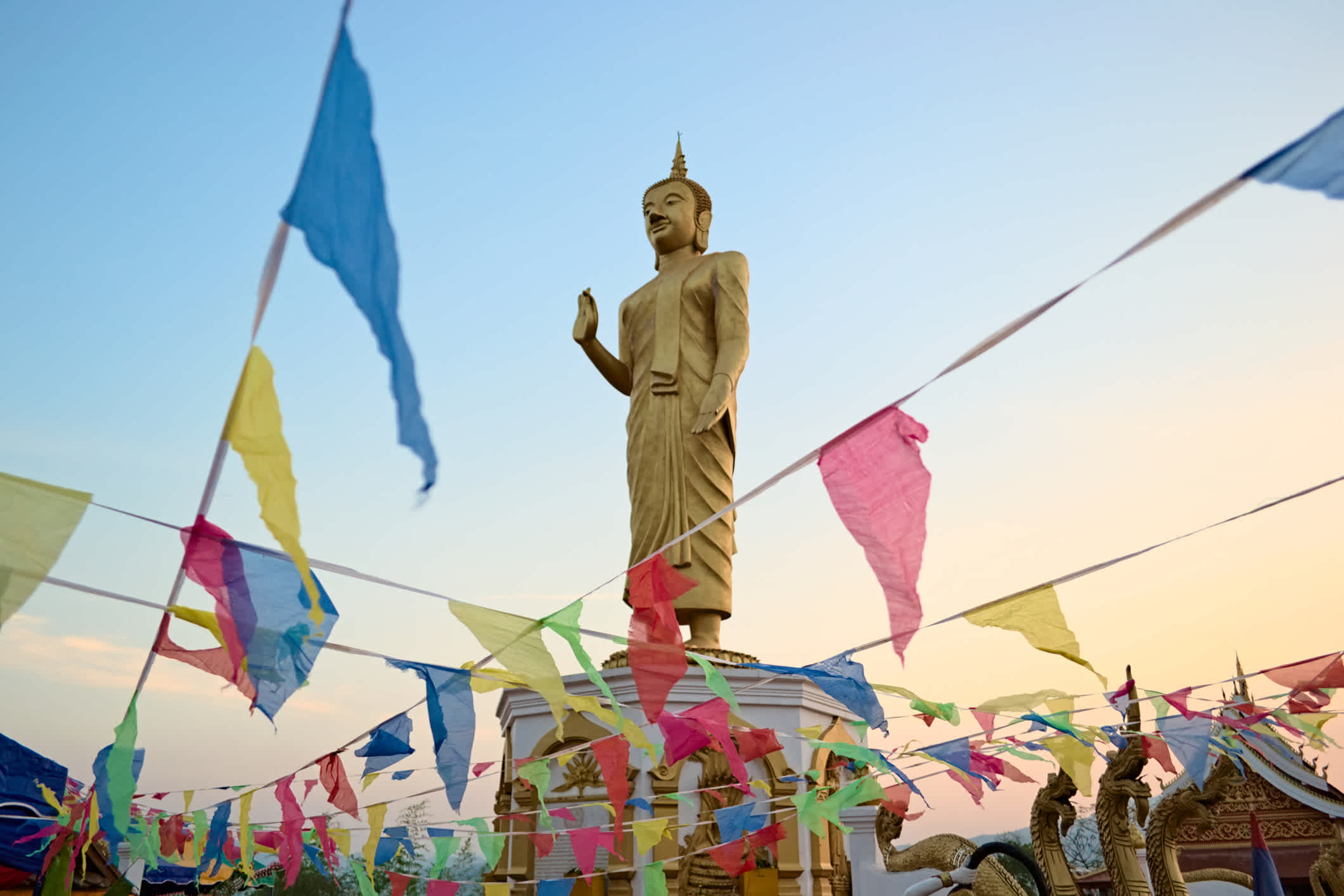 Statue de Bouddha en or debout entourée de fanions colorés, à Oudomxay, Laos