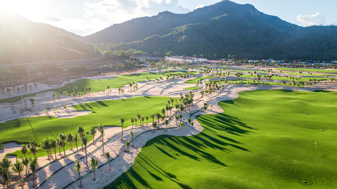 Weitläufiger Golfplatz mit grünen Fairways und Palmen, umgeben von Bergen. Vietnam.