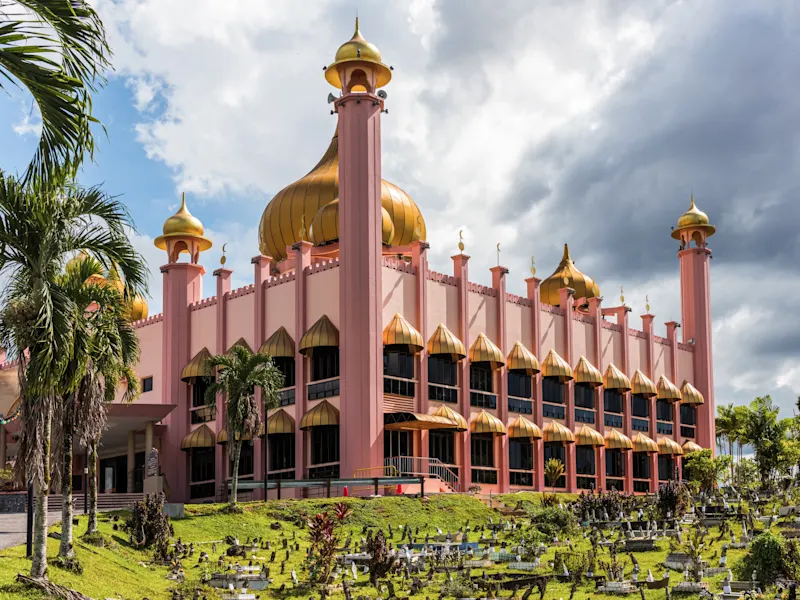 Rosafarbene Moschee mit goldenen Kuppeln und Palmen im Vordergrund. Kuching, Sarawak, Malaysia.
