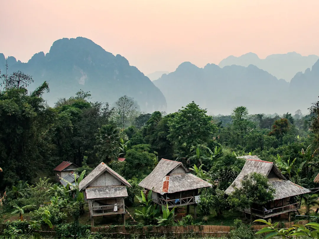 Laos, Vang Vieng Traditionelle Hütten im dichten Dschungel vor Bergen. Vang Vieng, Laos.
