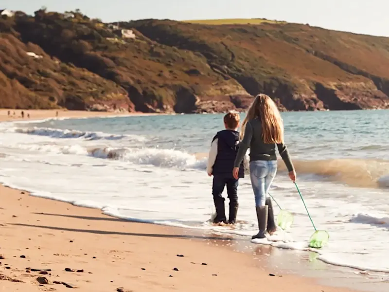 Wales, Familienurlaub Rückansicht der Familie mit Fischernetzen zu Fuß entlang der Küste des Winterstrandes. Wales, UK.