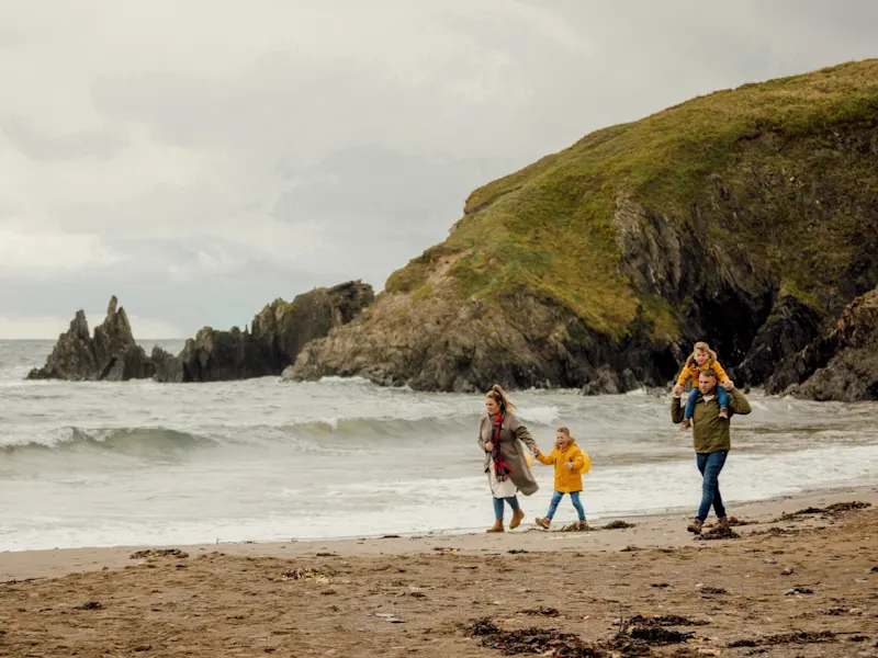 Rückansicht der Familie mit Fischernetzen zu Fuß entlang der Küste des Winterstrandes. Wales, UK.