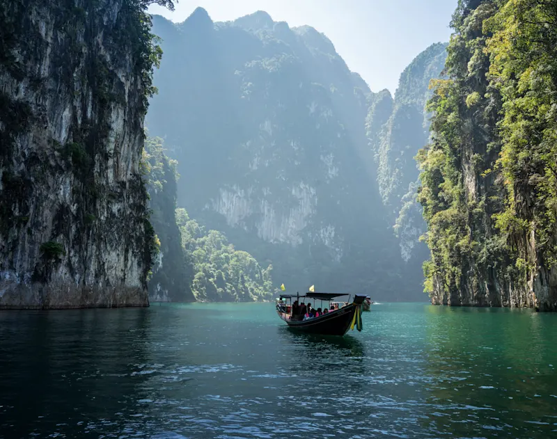 Khao Sok Nationalpark, Thailand Longtail-Boot auf türkisfarbenem Wasser zwischen hohen Felsen, Khao Sok Nationalpark, Thailand.