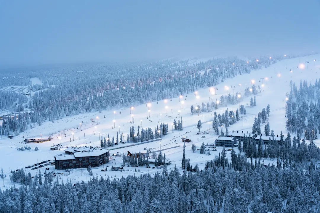 Ferienanlage und bei Einbruch der Dämmerung beleuchtete Skipisten, Ruka, Finnland
