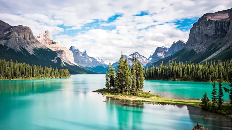 Idyllische Insel mit Bäumen im türkisfarbenen Maligne See, umgeben von beeindruckenden Bergen. Jasper Nationalpark, Alberta, Kanada.