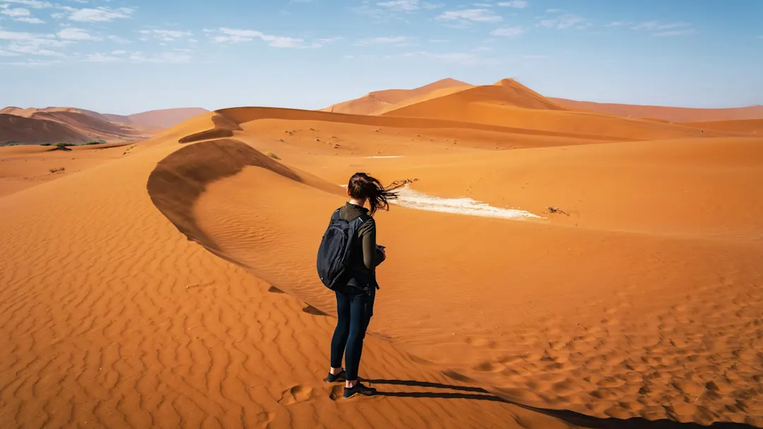 Frau mit Rucksack blickt auf hohe Sanddünen in der Wüste, Sossusvlei, Namib-Naukluft, Namibia.