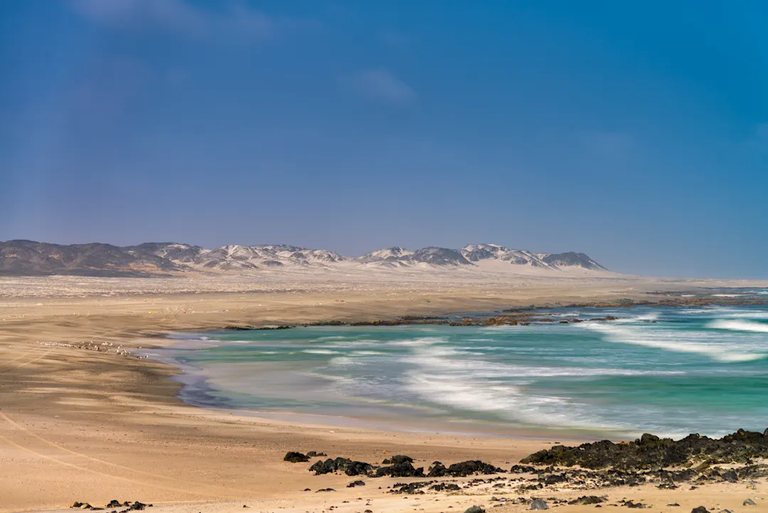 Weite Wüstenlandschaft, umgeben von sandigen Dünen und türkisfarbenen Wellen an der Küste, Ras Al Hadd Beach, Oman. 
