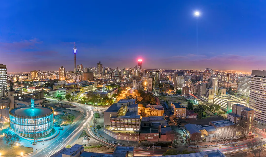 Johannesburger Stadtbild und Mondlicht, aufgenommen bei Sonnenuntergang, zeigt den beleuchteten Ratssaal, der das Zentrum für die Revitalisierung und Stadterneuerung des Bezirks sein wird. Hillbrow Wohngebiet und der prominente Kommunikationsturm und Ponte Wohnungen.