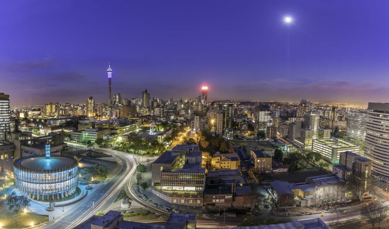 Johannesburger Stadtbild und Mondlicht, aufgenommen bei Sonnenuntergang, zeigt den beleuchteten Ratssaal, der das Zentrum für die Revitalisierung und Stadterneuerung des Bezirks sein wird. Hillbrow Wohngebiet und der prominente Kommunikationsturm und Ponte Wohnungen.