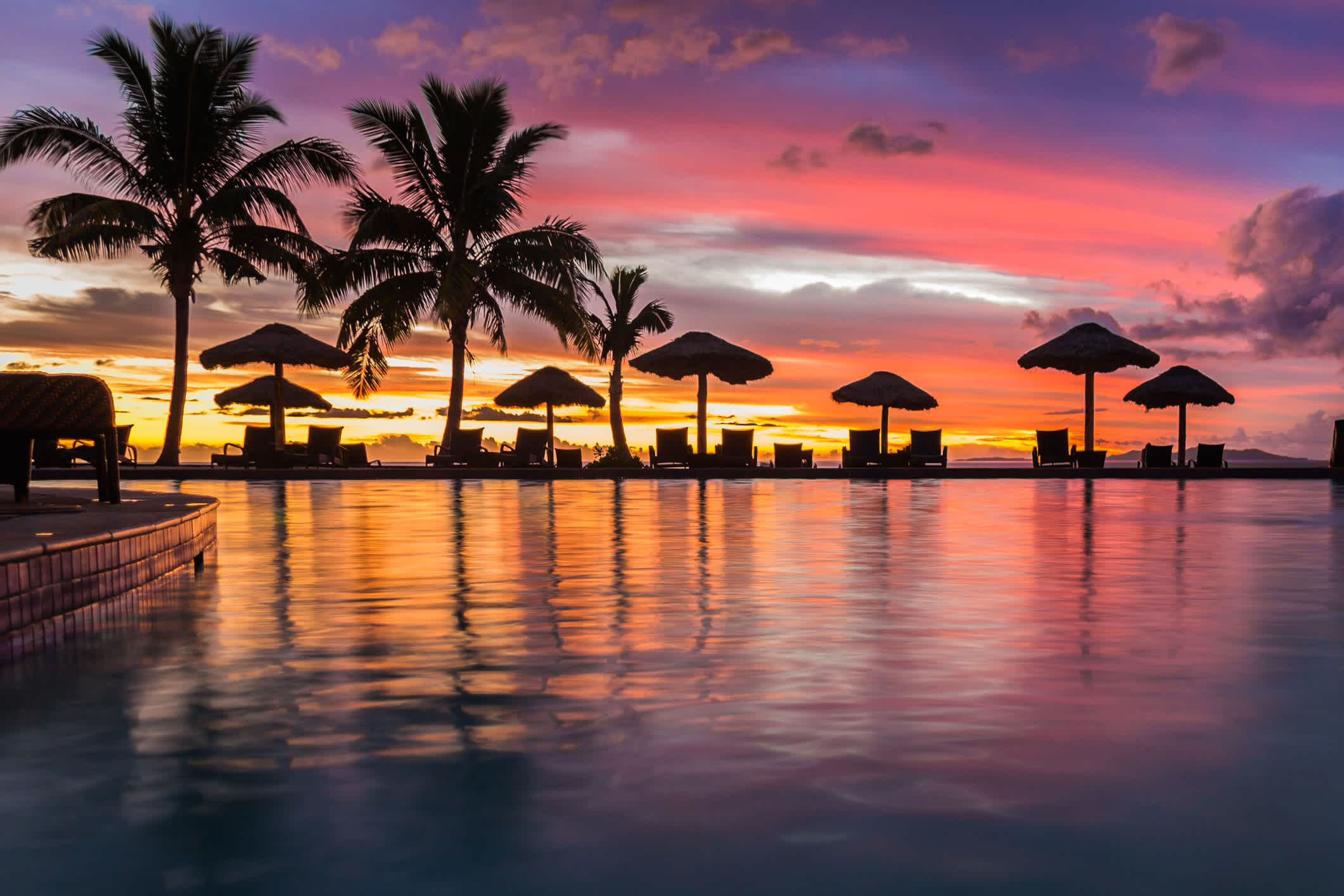 Transats sous des parasols au bord d'une piscine au coucher du soleil, île Denarau, îles Fidji
