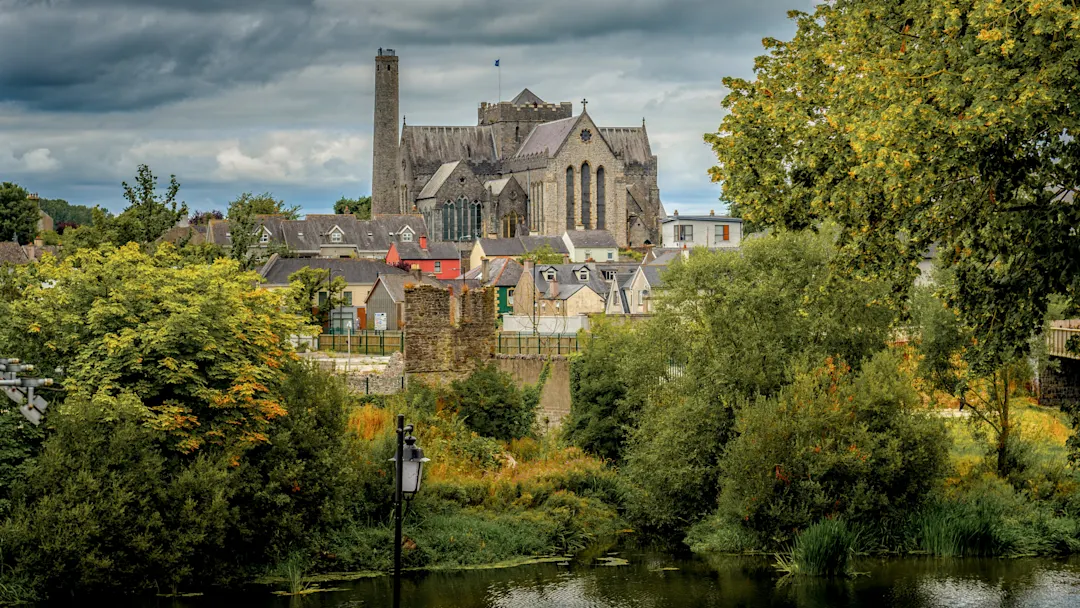 Blick auf die St. Canice's Cathedral in Kilkenny, Irland, mit grünen Bäumen und Wolken.