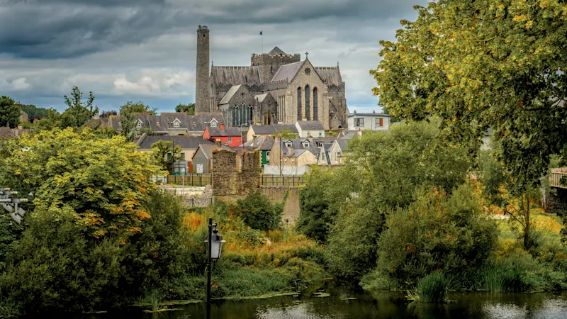 Blick auf die St. Canice's Cathedral in Kilkenny, Irland, mit grünen Bäumen und Wolken.